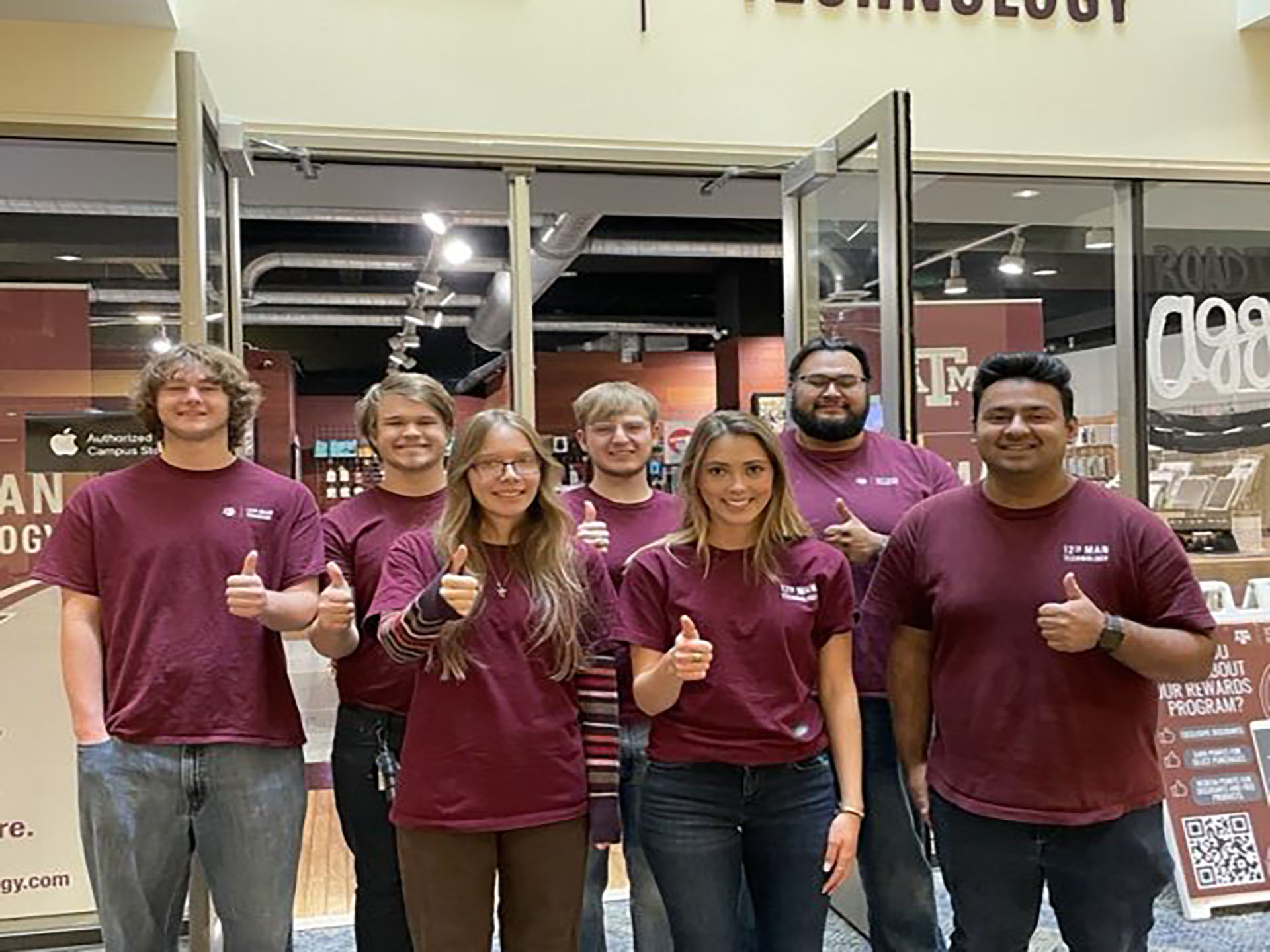 Group of Students inside the store front showing a thumbs up.